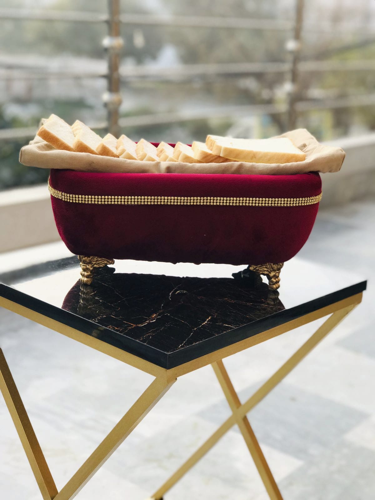 Red velvet bowl with gold trim holding bread slices on a black marble table.